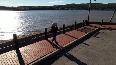 A-woman-walks-along-a-brick-paved,-boat-dock-in-upstate,-NY-on-a-sunny-morning
