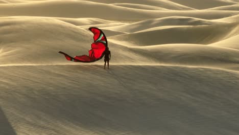 Man-with-red-colored-kite-standing-on-sandy-hill-and-watching-desert-of-Brazil-during-windy-day---aerial-orbit