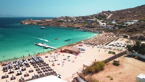 Aerial-orbit-shot-of-Super-Paradise-Beach-in-Mykonos-Greece-with-a-view-of-sea-clubs-restaurant-with-clean-sky-water