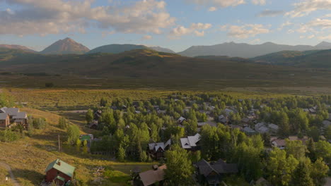 Aerial-push-over-houses-in-Crested-Butte,-Colorado-and-towards-the-Rocky-Mountains-on-the-horizon-on-a-beautiful-sunny-morning
