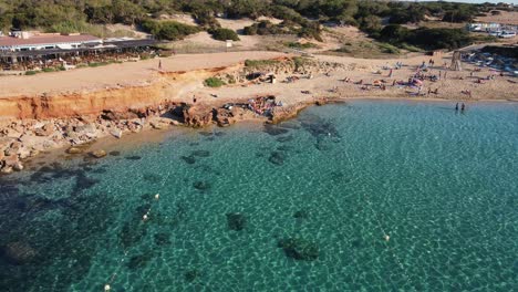 surfers-on-beach-at-Cala-Comte,-Ibiza-aerial-pullback-to-reveal-beauty