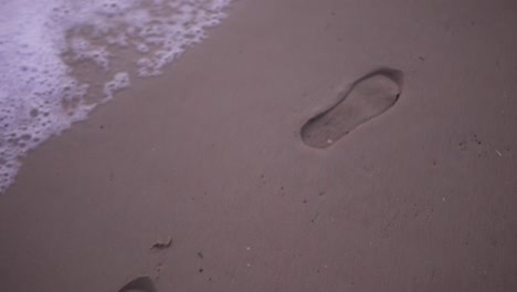 Slow-motion-tracking-shot-of-foot-prints-on-the-beach-with-waves-crashing