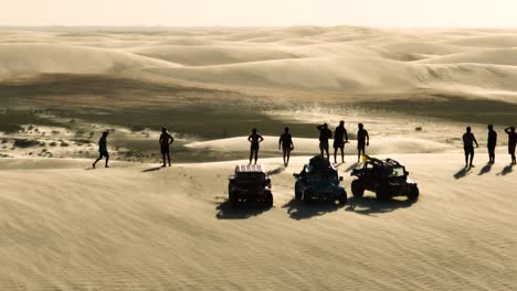People-in-silhouette-on-high-sand-dune,-windy-conditions-on-buggy-tour