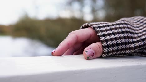 Woman-hand-with-beautiful-pink-nail-polish-design-on-handrail-outside-in-nature