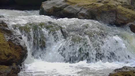 Slow-motion-shot-of-flowing-water-stream-on-rocky-river-in-nature,close-up