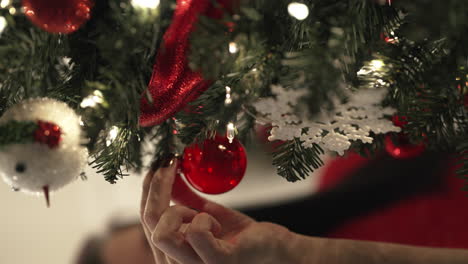 Close-up-pan-across-Christmas-tree-to-young-woman-hanging-ornament-on-branch---vertical-video
