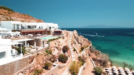 Super-Playa-Paradisíaca-En-Mykonos-Grecia-Toma-Aérea-Con-Un-Resort-Privado-Y-Bahía-En-Un-Día-Soleado