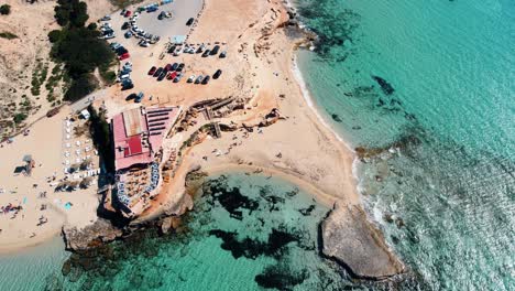 Cala-Comte-Ibiza,-overhead-view-of-resort-on-edge-of-crystal-clear-ocean