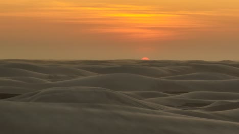 Leuchtend-Orangefarbener-Sonnenuntergang-über-Hügeliger-Sanddünenlandschaft,-Antenne-Links