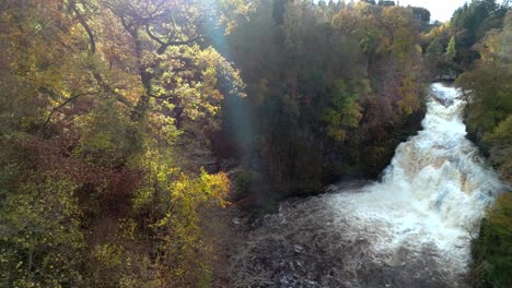 Slowly-twisting-drone-footage-of-a-cascading-waterfall-in-a-gorge-surrounded-by-colourful-trees-in-autumn