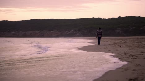 Slowmotion-shot-of-a-man-walking-alongside-the-ocean-during-sunset