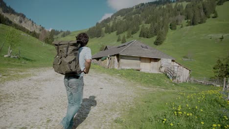 Gimbal-Tracking-Backpacker-In-Freizeitkleidung,-Der-Auf-Einer-Ländlichen-Schotterstraße-In-Einem-Bergtalweg-Zu-Einem-Haus-Wandert