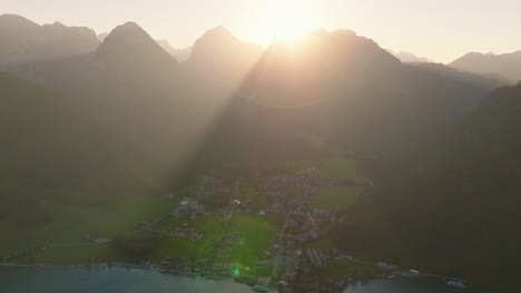 Pertisau-village-on-the-Achensee-lake-with-sunrays-glowing-through-Tyrol-alpine-mountain-range-peaks-aerial-view