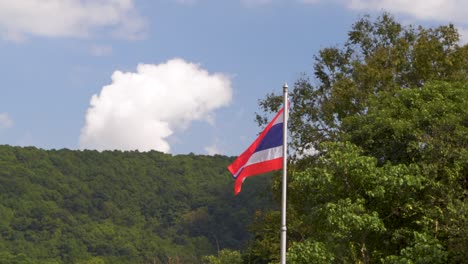 Thailändische-Flagge,-Die-Gegen-Blauen-Himmel-Und-Grün-In-Der-Natur-Weht