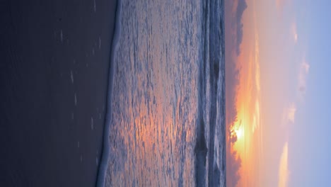 Beautiful-sunset-on-the-background-of-Baltic-sea,-sun-going-beyond-the-horizon-illuminating-water-and-clouds-in-the-sky,-calm-sea-waves,-romantic-mood,-copy-space,-vertical-shot