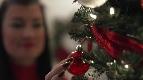 Close-up-pan-across-Christmas-tree-to-young-woman-hanging-ornament-on-branch---vertical-video