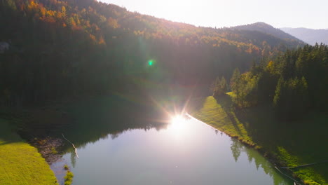 Hazy-woodland-mountain-sunrise-reflection-shining-in-Sylvenstein-forest-lake-aerial-view-dolly-right