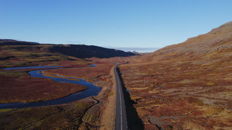 Carretera-Interior-Vacía-En-Islandia-Rodeada-De-Un-Paisaje-De-Follaje-Otoñal-Rojo-Con-Río-Azul-Y-Cielo-Despejado