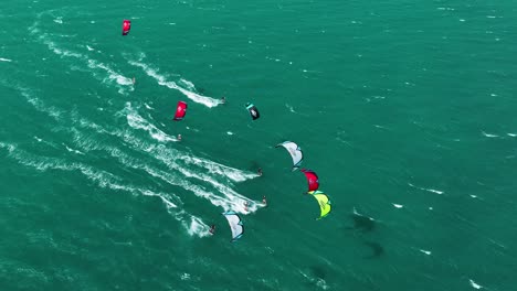 Aerial-top-down-showing-group-of-colorful-kites-and-kite-surfer-speeding-over-ocean-in-summer