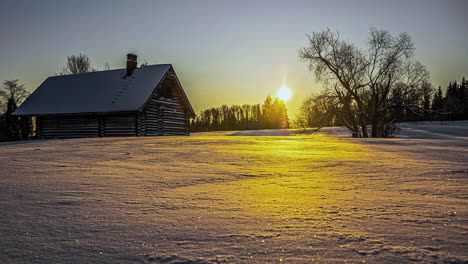 Goldener-Sonnenaufgang,-Der-Sich-Auf-Einem-Feld-Aus-Frischem-Schnee-Und-Einer-Hütte-Auf-Dem-Land-Widerspiegelt---Zeitraffer