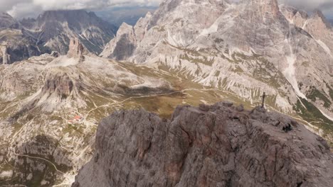 Aerial-backwards-shot-over-peak-of-Monte-Paterno-Mountain-with-cross-and-beautiful-landscape-during-summer---Sea-in-the-valley-in-Dolomites,Italy