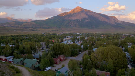 Aerial-landscape-of-Crested-Butte,-Colorado-on-a-beautiful-summer-evening-at-golden-hour-with-a-boom-down-towards-the-houses-and-street-below