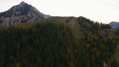 Rising-aerial-view-golden-sunrise-emerging-behind-extreme-rocky-Tyrol-woodland-alps-mountain-range-peaks,-Austria