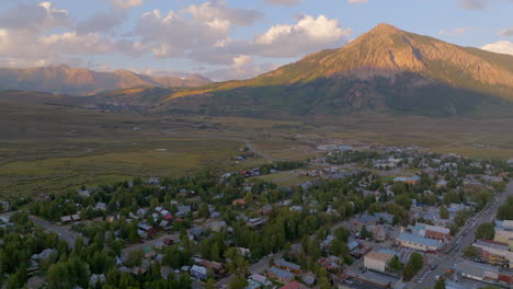 Aerial-with-pull-back-over-town-of-Crested-Butte,-Colorado-and-away-from-the-mountains-on-a-pretty-summer-day-at-sunset