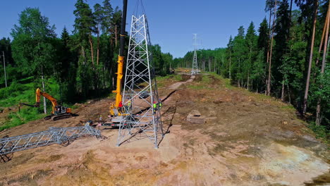 Crane-and-crew-erecting-a-powerline-pylon-tower-through-a-forested-wilderness---aerial-view