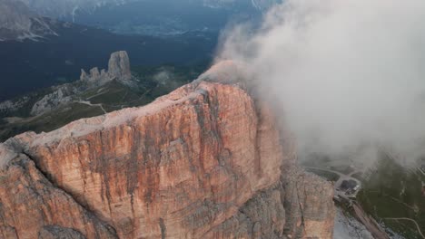 Dense-Clouds-covering-rocky-summit-of-Averau-Peak-in-Dolomites,-with-Cinque-Torri-towers-in-the-background-at-sunset