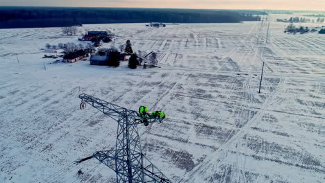Engineers-working-high-on-the-power-lines-of-an-electric-transmission-tower-in-the-winter-countryside---aerial-parallax
