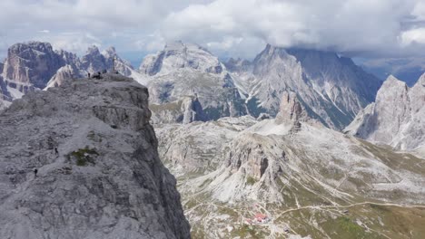 Aerial-panning-shot-showing-via-ferrata-climber-and-cross-on-the-peak-of-Monte-Paterno,-at-Tre-Cime,-in-the-Dolomites