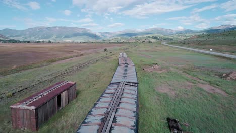 Drone-view-of-an-abandoned-train-on-the-countryside-of-Colorado-with-green-mountains-in-the-background
