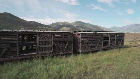 Drone-view-of-an-abandoned-wood-train-on-countryside-of-Colorado-with-green-mountains-in-thebackground