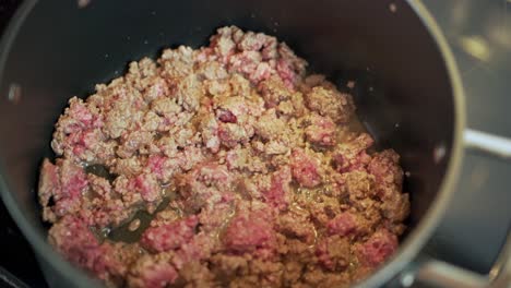 Cooking-bolognese-recipe-from-adding-and-browning-beef-to-adding-sauce,-lots-of-stirring-and-lifting-of-lid-with-steam,-black-pot