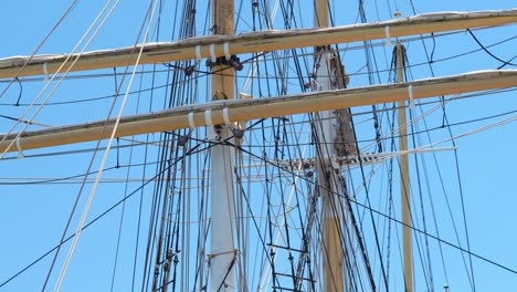 Tall-ship-rigging-gently-swaying,-backlit-against-a-clear-blue-sky,-showing-three-masts-and-crow's-nest