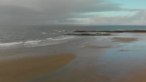 Drone-shot-moving-over-small-waves-rolling-in-on-Scottish-shore