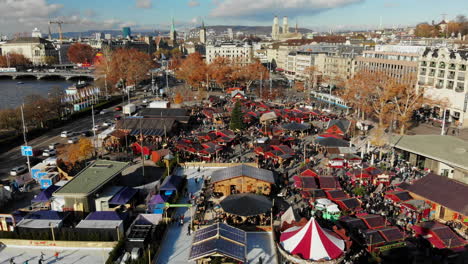 Drone-shot-lowering-over-the-Christmas-Market-revealing-angel-statue-above-the-Opera-House-in-Zurich,-Switzerland-during-the-day-with-the-cityscape-in-the-background