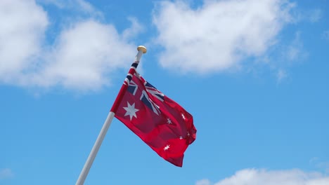 Australian-Red-Ensign-flag,-flying-against-a-bright-blue-sky-with-fast-moving-clouds