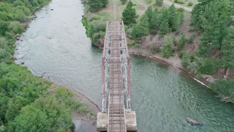 Drone-view-of-a-railroad-bridge-going-over-a-green-river-in-Colorado