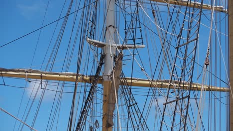 Tall-ship-rigging-gently-swaying,-frontlit-against-a-blue-sky-and-few-clouds