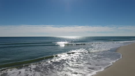 Drone-shot-flying-towards-gentle-ocean-waves-crashing-along-the-sandy-beach