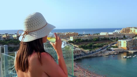 Chica-Bebe-Una-Copa-De-Vino-Con-Vistas-A-Una-Hermosa-Playa-Mientras-Está-De-Vacaciones-En-Malta