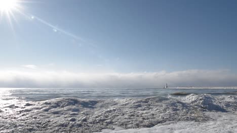 Strand-Im-Winter-Mit-Eis-Und-Schnee-Bedeckt,-Mit-Einem-Leuchtturm-In-Der-Ferne