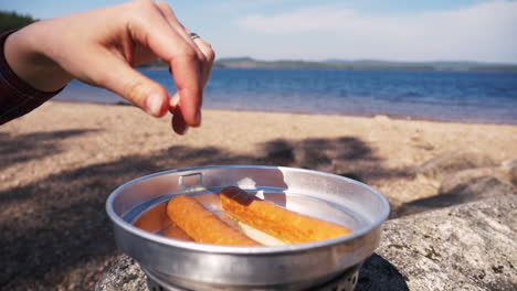 Close-up-of-girl-putting-sausage-in-a-pan-of-a-Trangia-portable-stove
