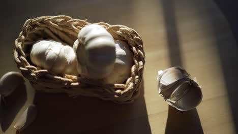 Garlic-in-basket-on-wooden-table-some-cloves-separated,-sunshine-creating-shadows-on-table