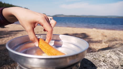Close-up-of-girl-putting-sausage-in-a-pan-of-a-Trangia-portable-stove