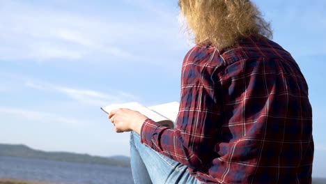Girl-sitting-and-reading-a-book-at-a-lake-on-a-sunny-day
