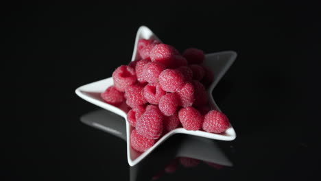 Vibrant-red-raspberries-in-white-star-dish-on-black-table-with-movement-from-left-to-right