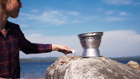 Swedish-girl-puts-on-the-pan-of-a-Trangia-portable-stove-to-cook-at-the-lake